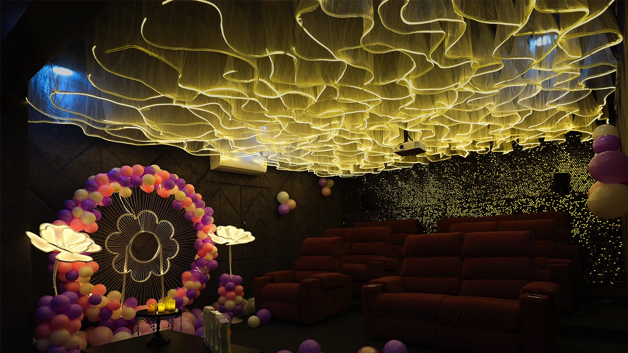 Luxury private theatre room with glowing ceiling design, balloon decoration arch, cozy recliner seating, and ambient lighting set for a celebration or special event.